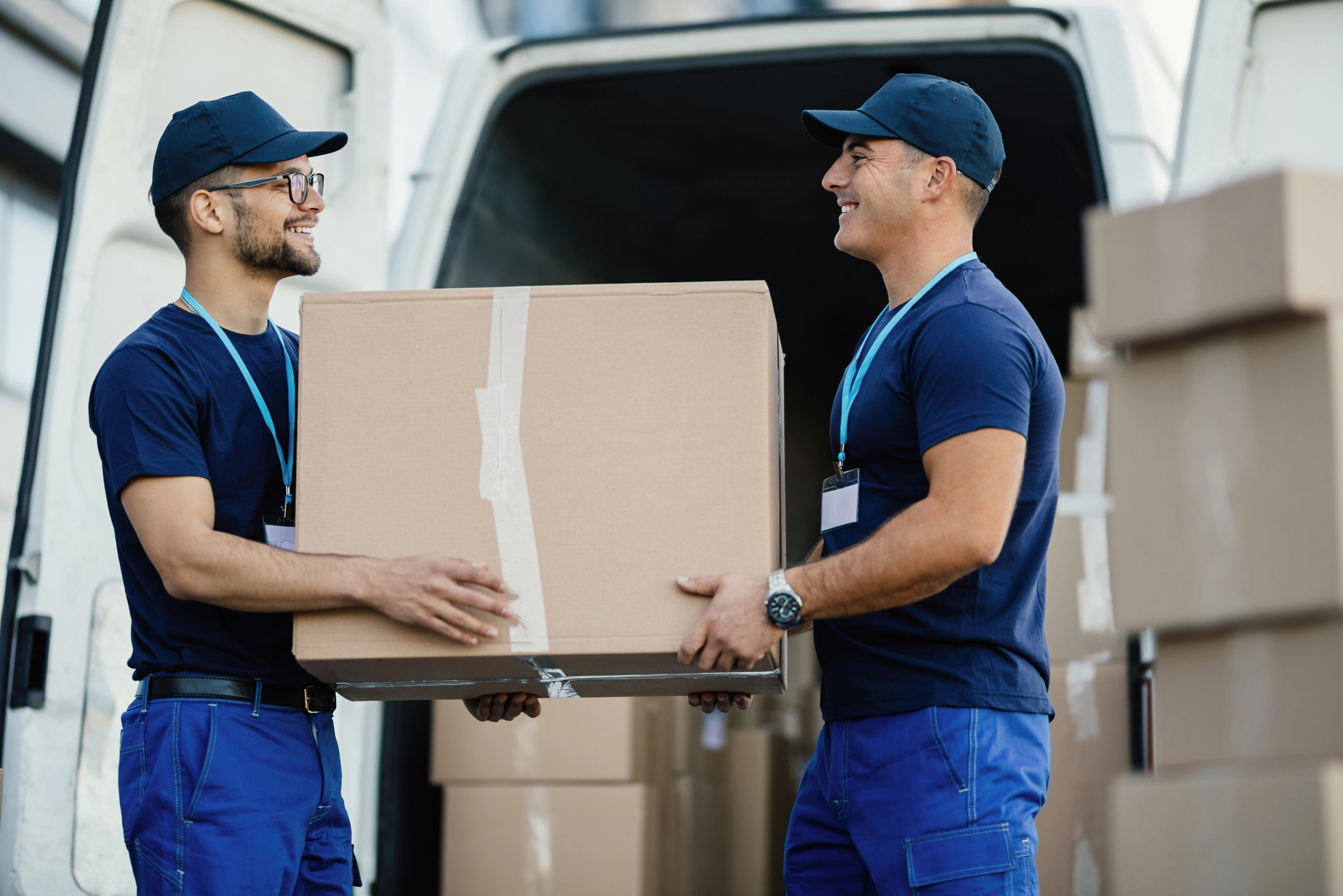 Happy delivery men unloading cardboard box from a mini van.