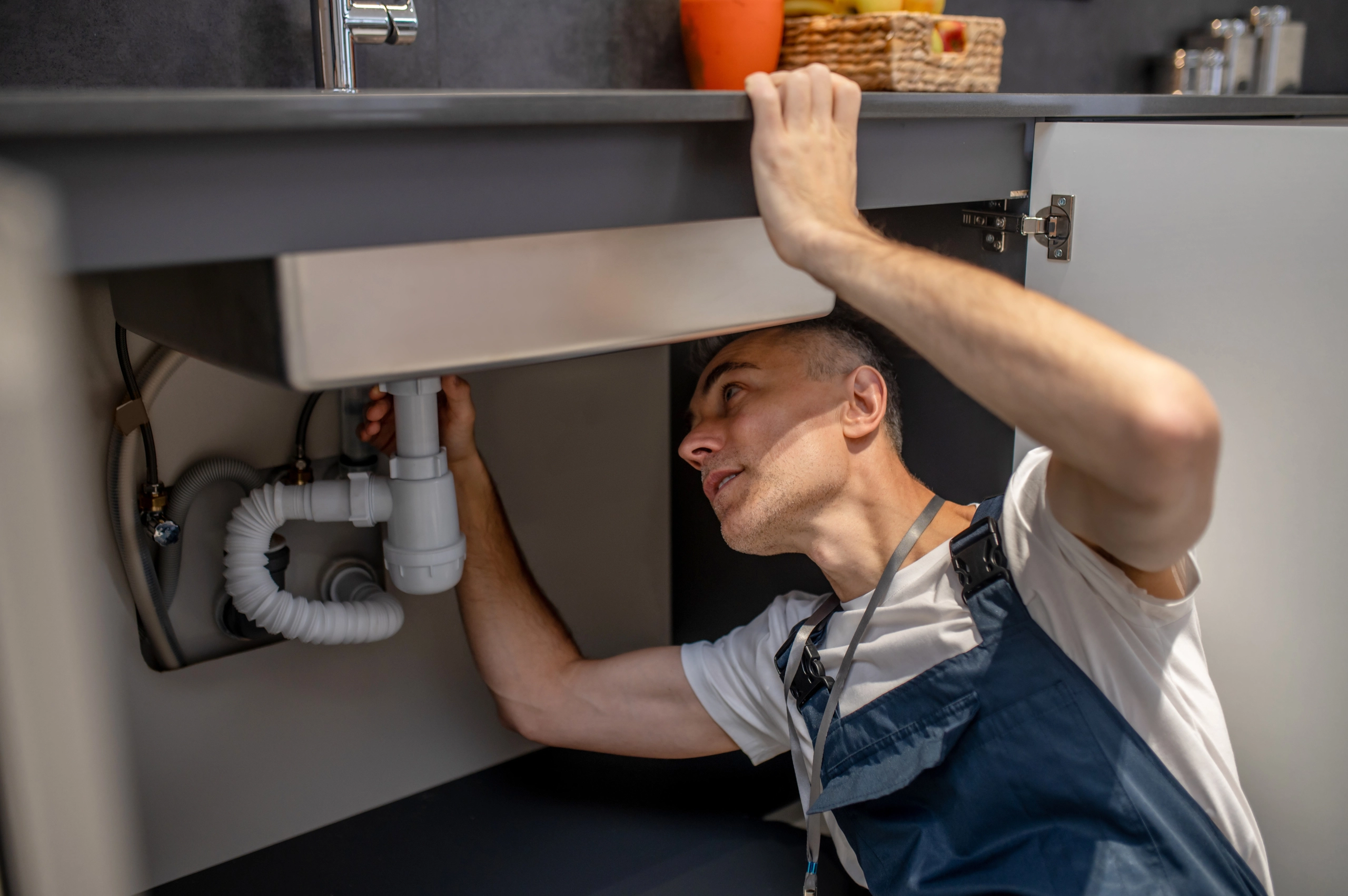 Man carefully examining bottom of sink and pipe